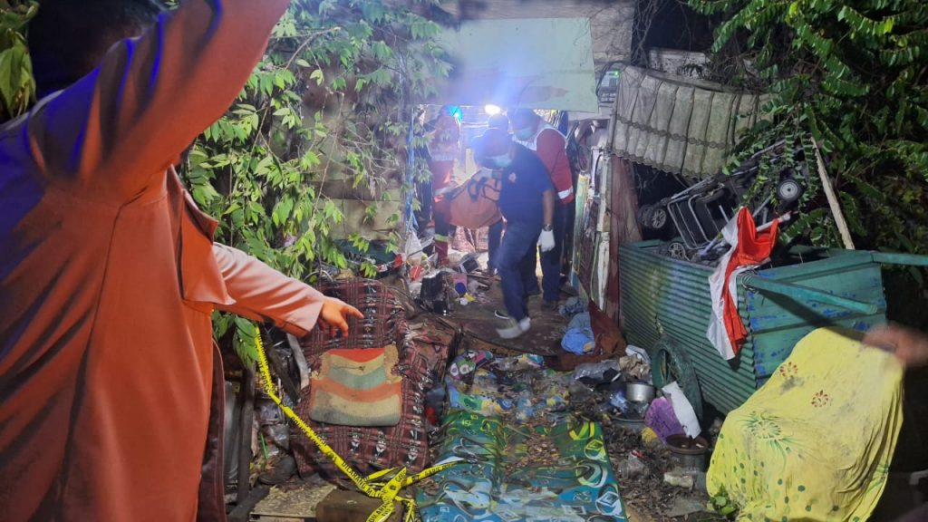 Petugas mengevakuasi jasad seorang pria lanjut usia yang ditemukan meninggal di dalam gubuk tempat tinggalnya, Senin (13/10/2025) sore.